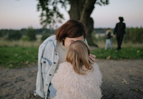 A tender moment between mother and daughter outdoors in a grassy field at twilight.